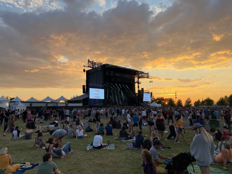 People sit near a music festival stage at sunset.