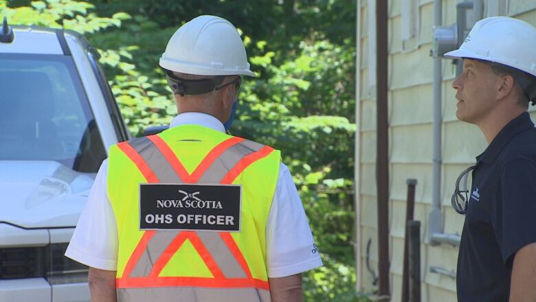 Two men are standing next to each other wearing white hard hats.