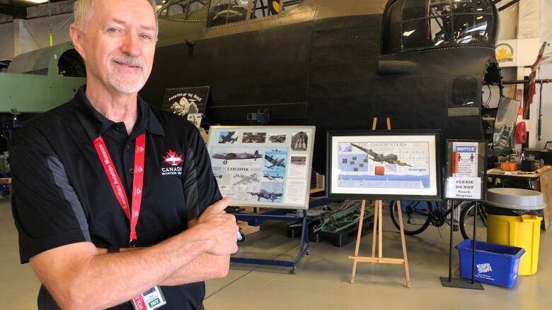 A man standing arms-crossed in front of a Second World War plane