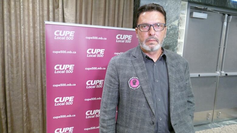 A man stands before a pink CUPE Local 500 banner, wearing a pink sticker that says 