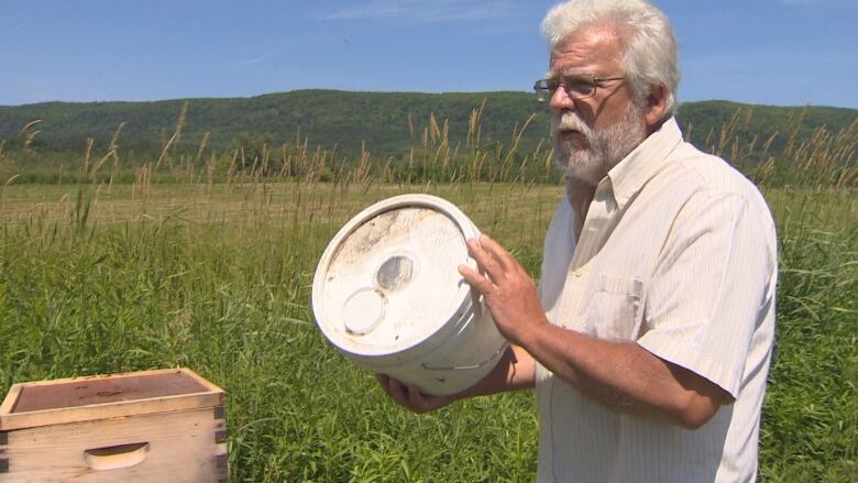 Bill McKee holds a white barrel with a hole in the top that is covered by mesh.