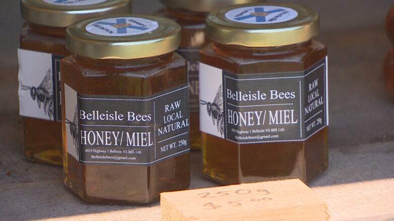 Two jars of honey with the label Belleisle Bees sit for sale on a shelf. 