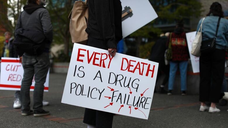 A protester holds up a sign that reads 'Every Death is a Drug Policy Failure'.