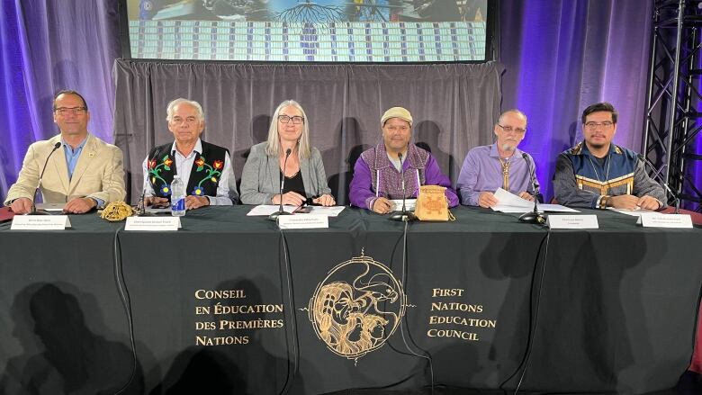 Six people sit behind a table with the logo of the First Nations Education Council.