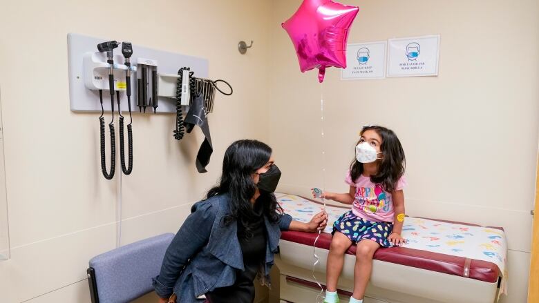 A mother and daughter sit in a doctor's office. The daughter is holding a balloon.