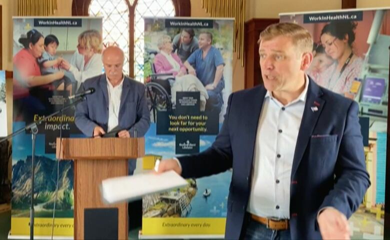 Premier Furey speaks to a woman not in frame during a press conference. His arms are in the air as he explains.