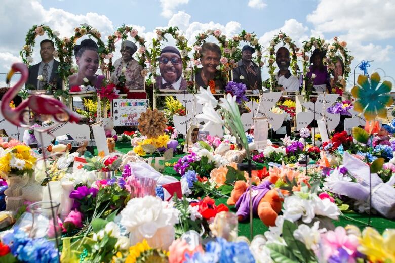 Flowers and other items are strewn in front of a memorial for 10 people.