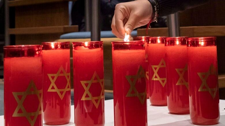 Someone lighting red candles with the star of David with a match. 