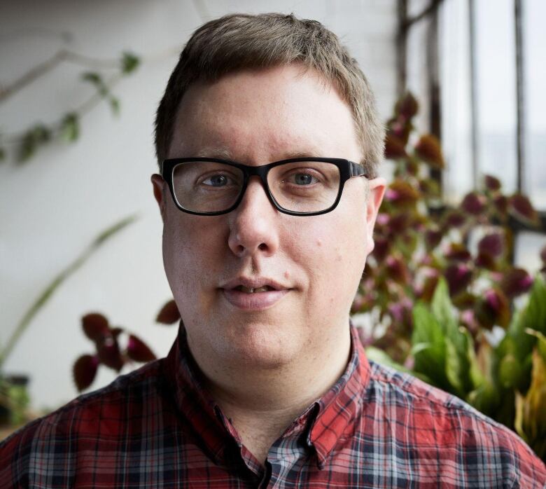 Aaron Lakoff wearing a red and grey plaid shirt and black rectangular glasses.