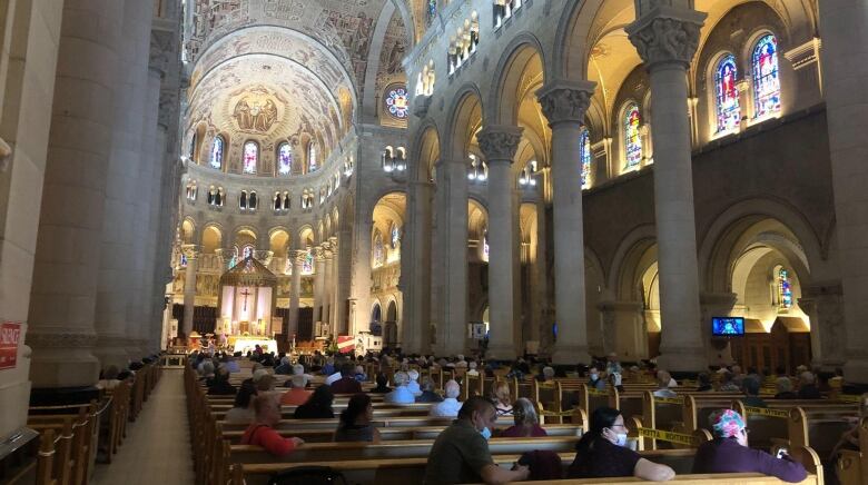 Picture shows the inside of a basilica, with people seated on church benches.