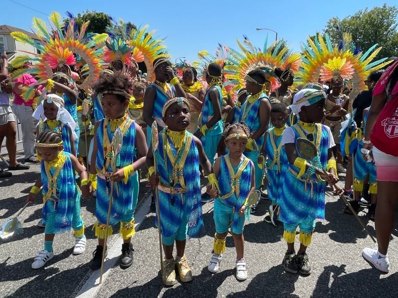 Five children in colourful costumes stand in front of a crowd of people.