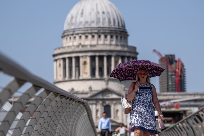 A woman in a floral pattern dress holds an umbrella over her head while walking on a bridge.