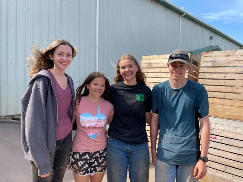 A group of four smiling kids/teens standing outside - 3 girls and a boy. 