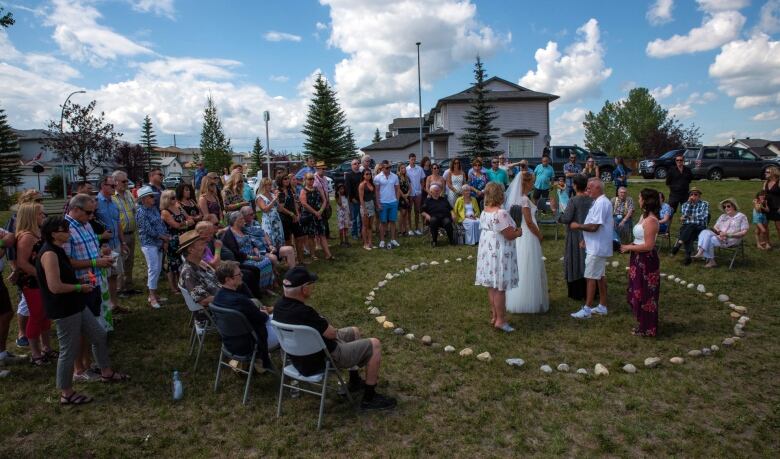 A wedding ceremony takes place outdoors inside a circle of rocks in a park. 