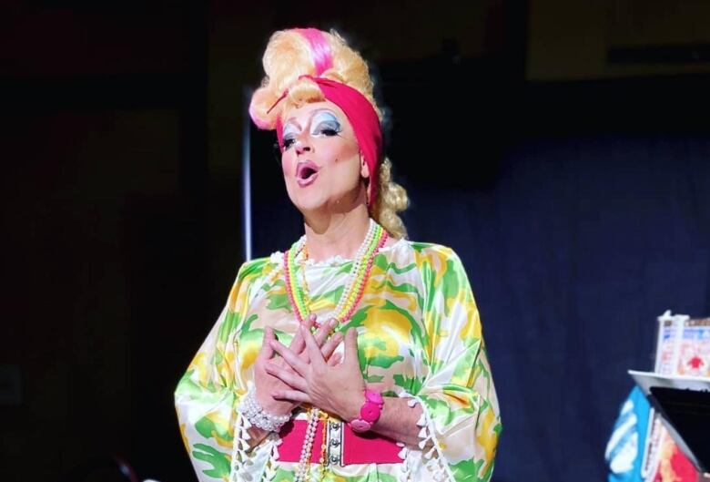 A drag performer in a blonde wig and a bright dress sings. 