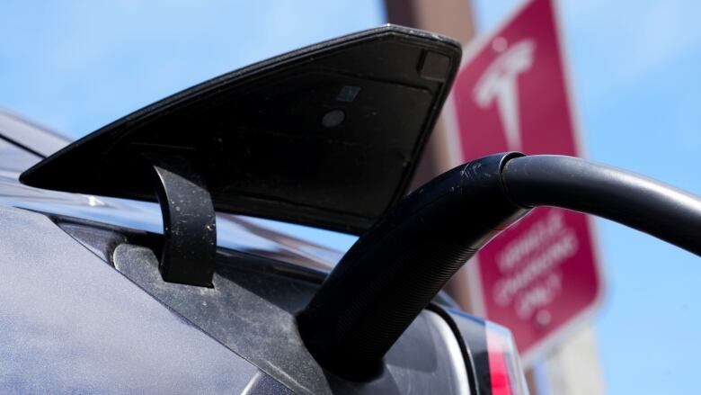 An electric vehicles is plugged in near a Tesla sign.