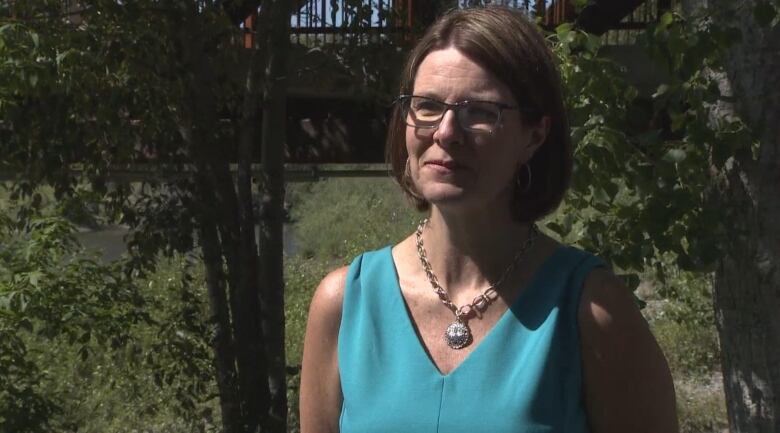 A woman with a short brown bob is wearing a turquoise shirt. 