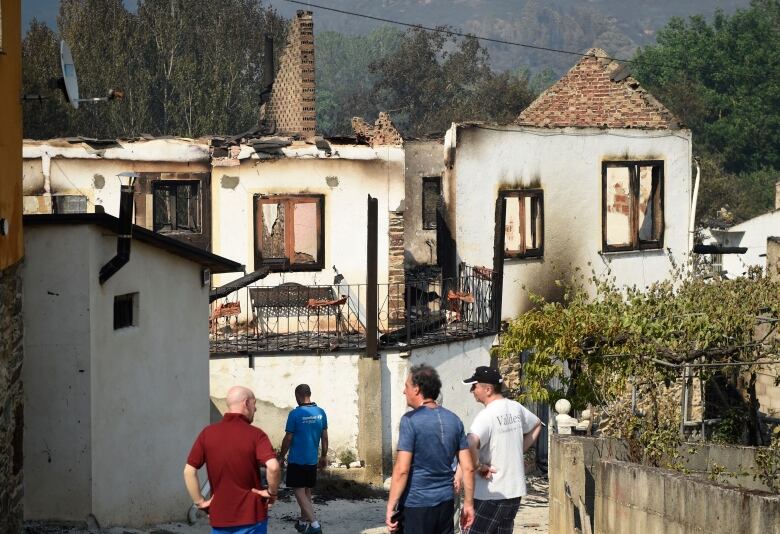 Four men stand in front of a line of burnt-out houses.