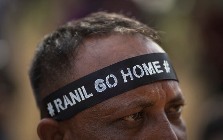 A man wears a headband saying 'Ranil go home'