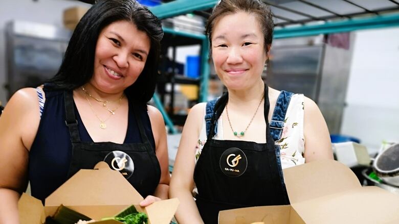 Two women pose for a photo with takeout food boxes.