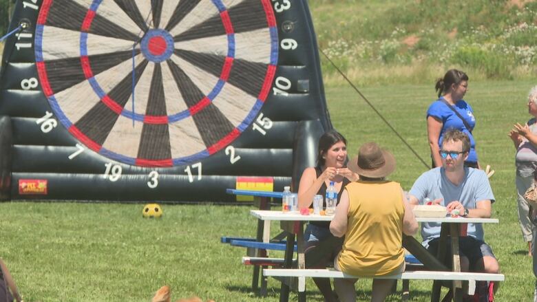 People picnicking, and a giant inflatable soccer ball target formed like a dart board.