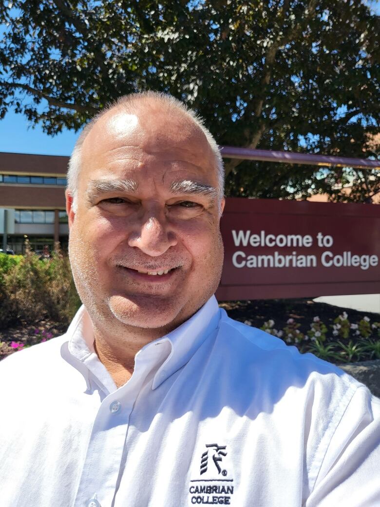 A man in front of a sign that says Cambrian College.