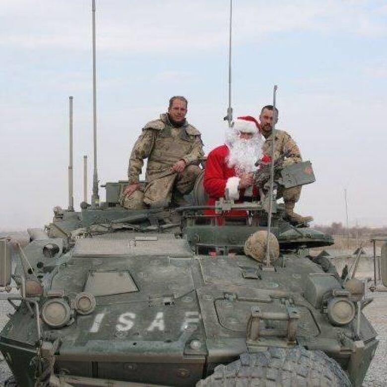 Two uniformed soldiers ride on a tank with Santa Claus. 