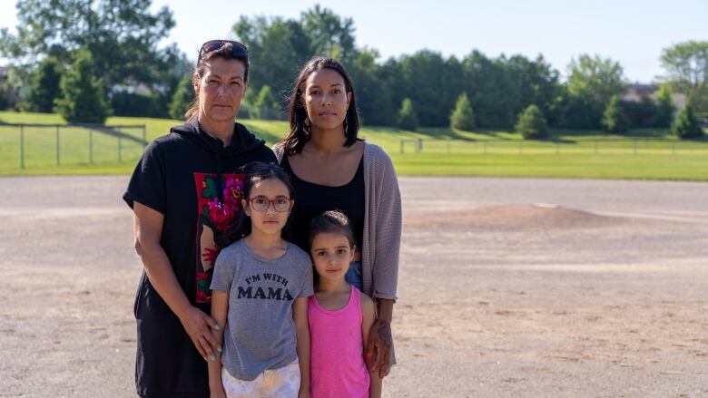 A mom, grandmother, and two young girls pose on a baseball field.