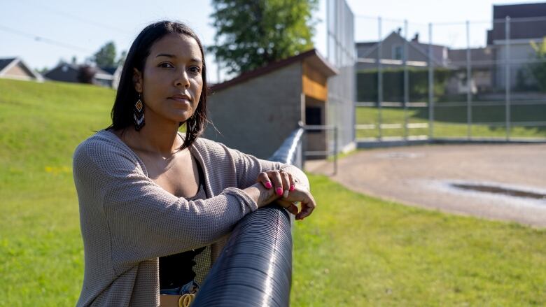 A woman leans on a fence at a baseball diamond.