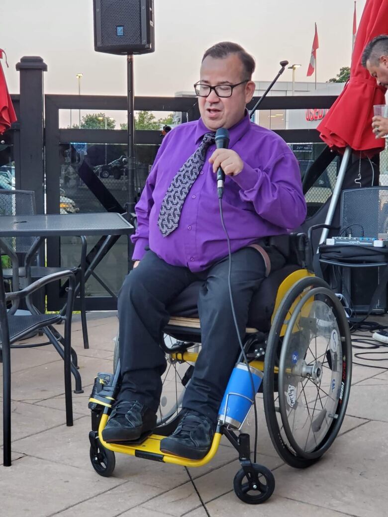 A man sits in a wheelchair and speaks into a microphone. 