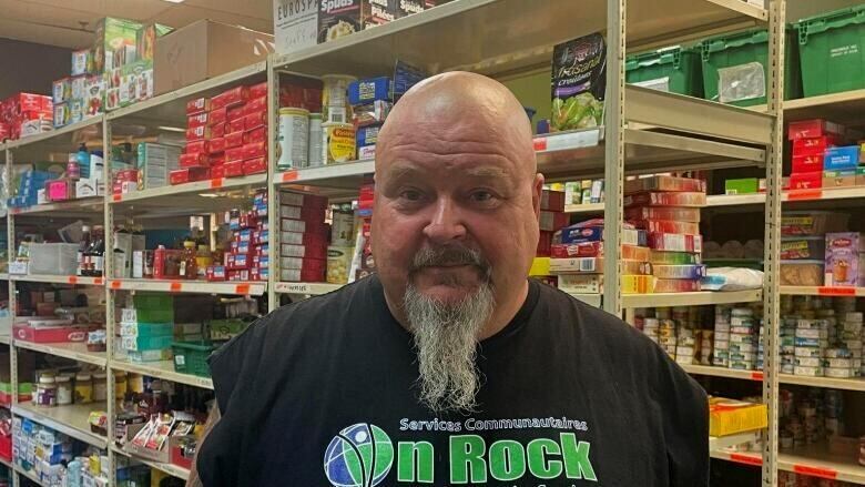 Man in Tshirt standing in front of shelves of food.