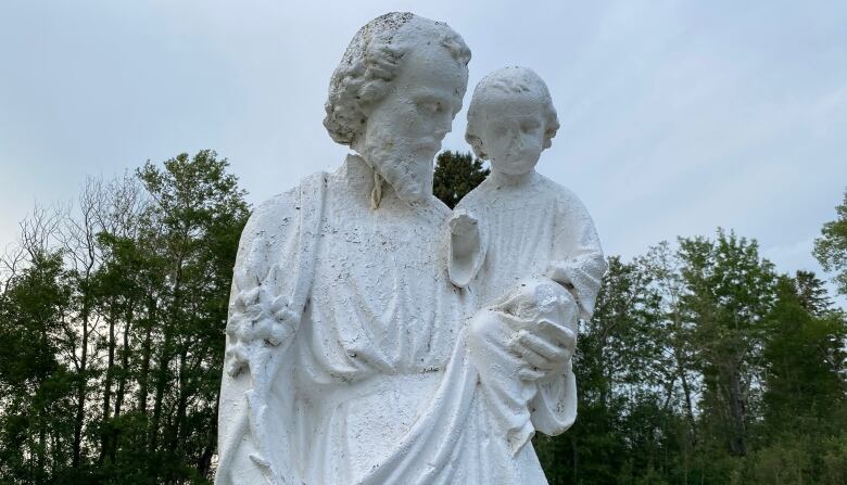 A white stone statue depicts a robed man cradling a small child in one arm.