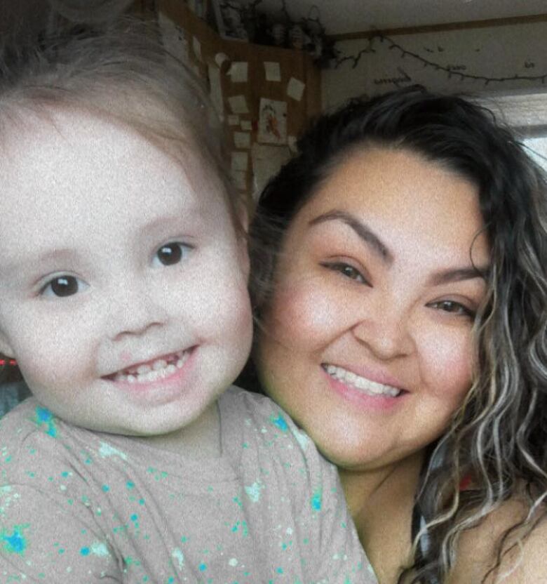 A woman holds a toddler as they both smile.