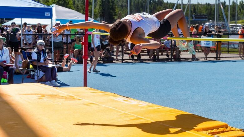 A young person in a ponytail competes in a high jump competition.