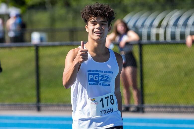 A young man on a track gives a thumbs up to the camera.