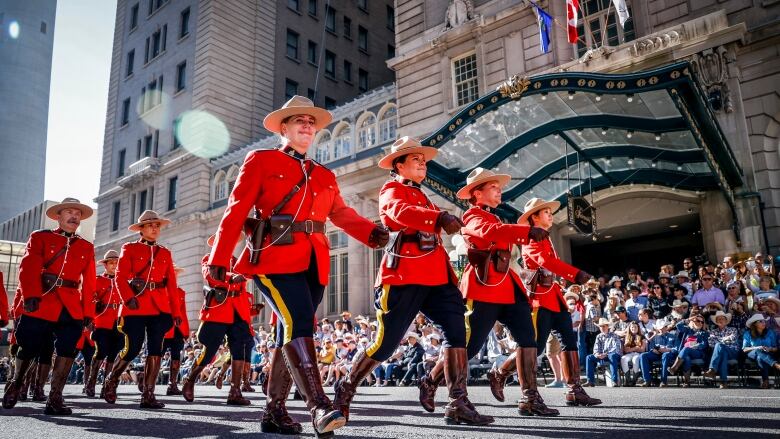 rcmp officers in red uniforms and cowboy hats march at parada