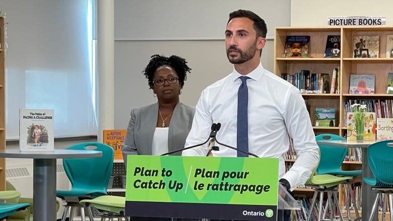 Stephen Lecce standing at a podium with a sign that says 'Plan To Catch Up.'