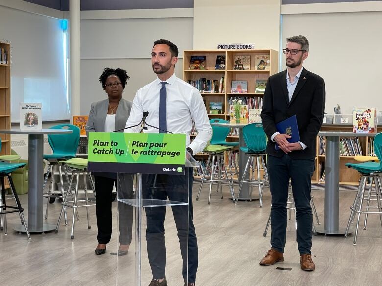 Stephen Lecce standing at a podium with a sign that says 'Plan To Catch Up.'