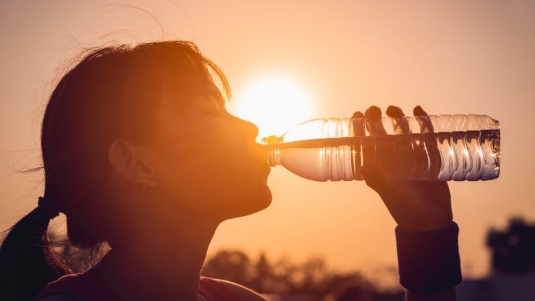 Woman drinking from water bottle with sun behind her, creating a silhouette