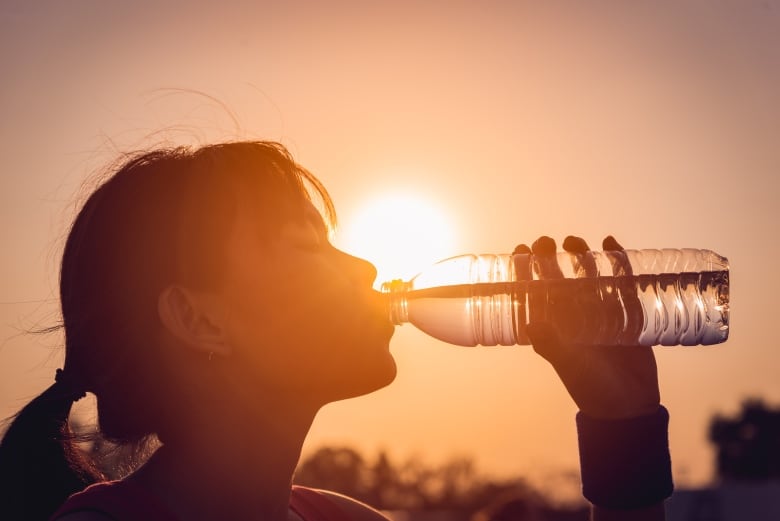 Woman drinking from water bottle with sun behind her, creating a silhouette