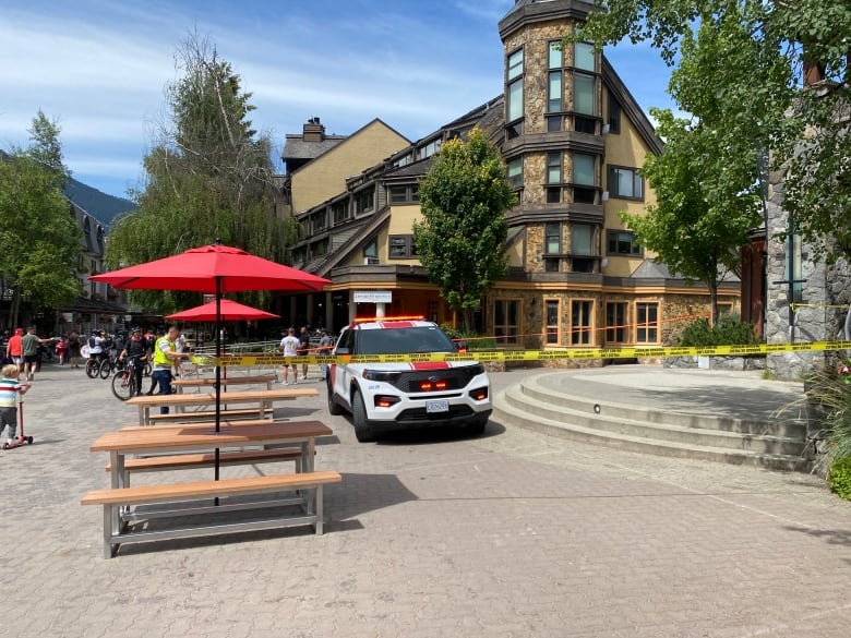 A red car with a siren on it behind police tape in a pedestrian plaza.