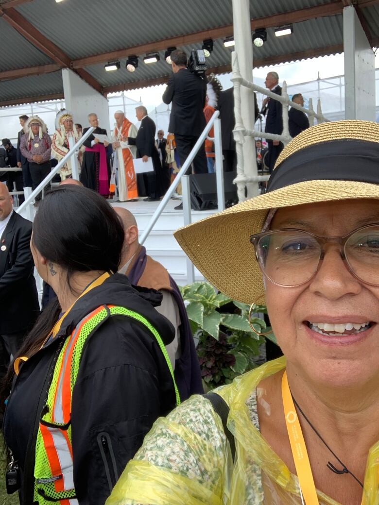 A portrait of a woman within a crowd of people. The pope is distantly in the background.