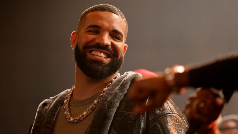 A close up image of a bearded man, wearing a thick gold chain smiling broadly towards the camera. 