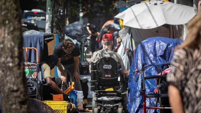 A person in a wheelchair rolls past tents on a sidewalk.