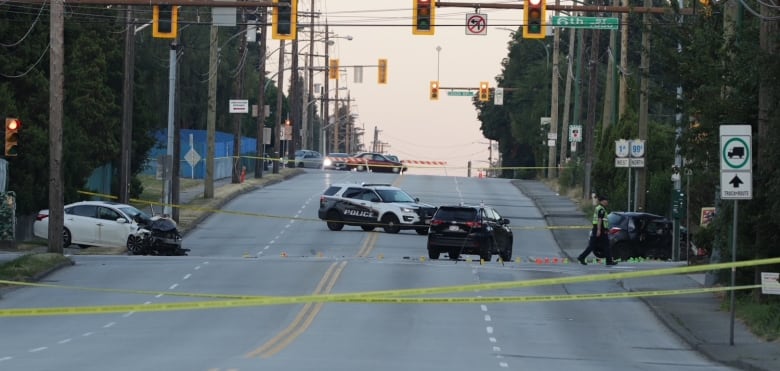 Two crashed cars sit behind a police line on a wide street.