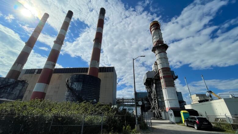 power plant with four large, red-and-white stacks extending into the air with a bright blue sky in the background.