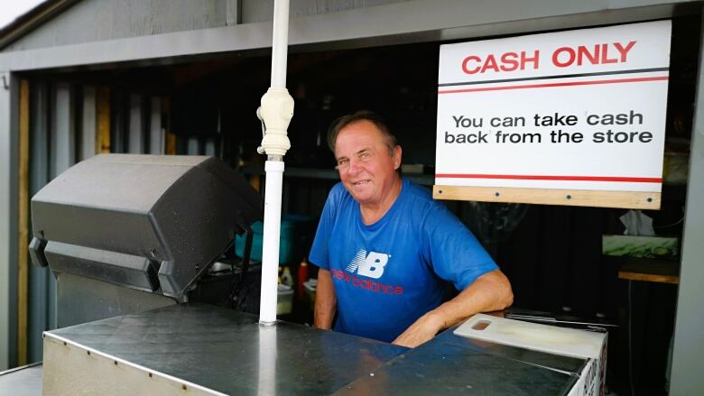 Man stands behind silver counter and black BBQ. A sign behind him says 