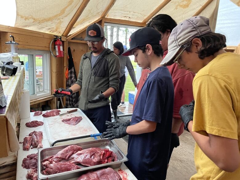 People standing next to a table with deer meat on it.