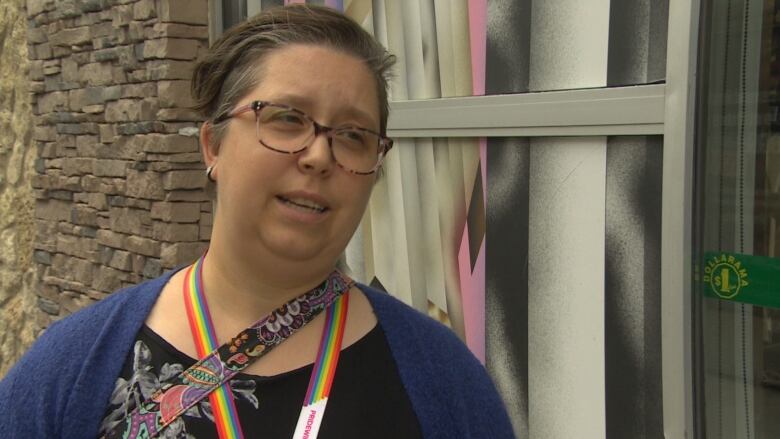 A woman with short hair and glasses speaks in front of a store.