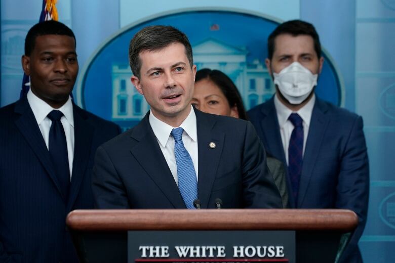 A man speaks at a lectern, flanked by aides.